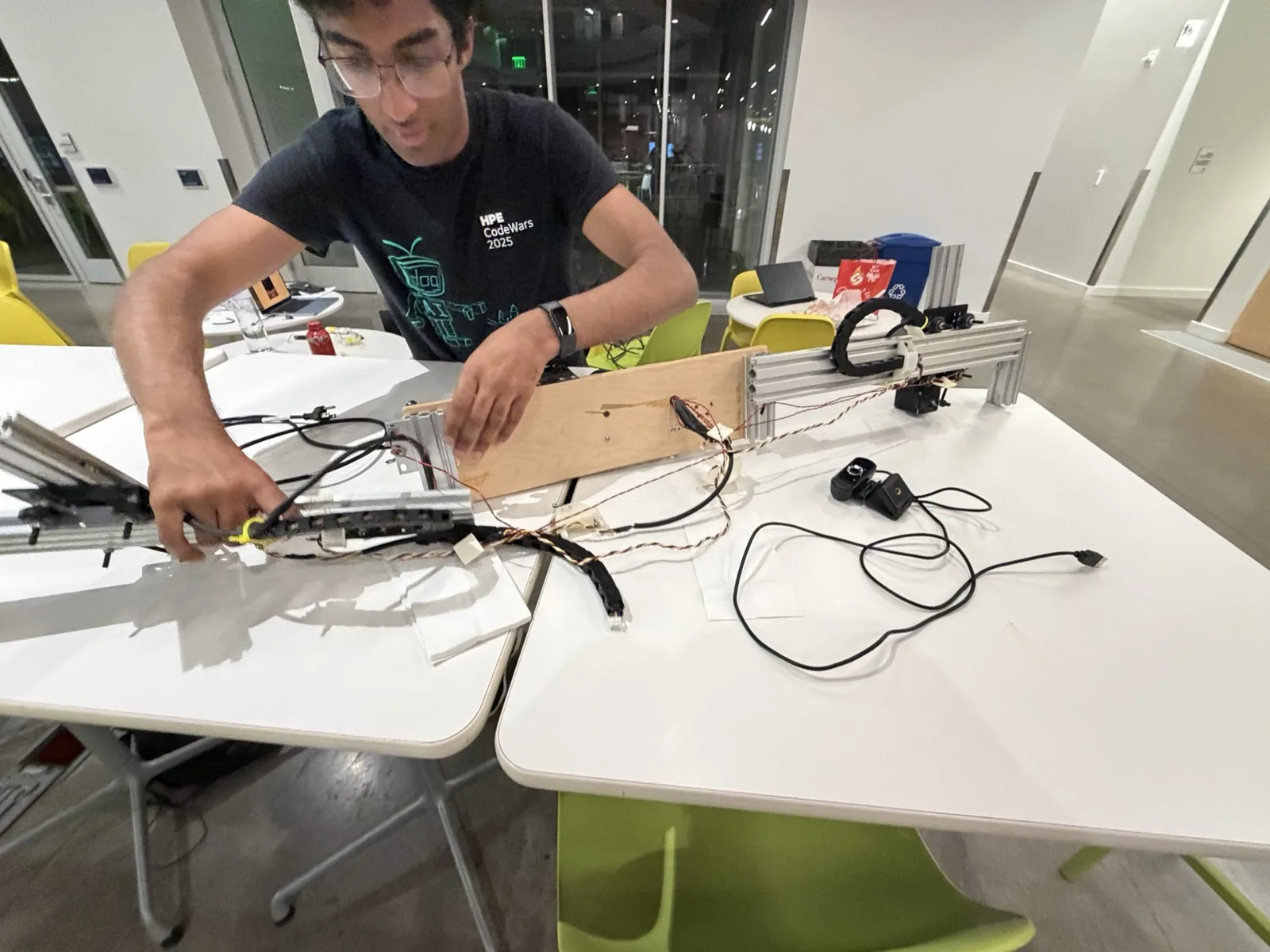 A teammate leaning across two tables, wiring up the aluminium extrusion rails