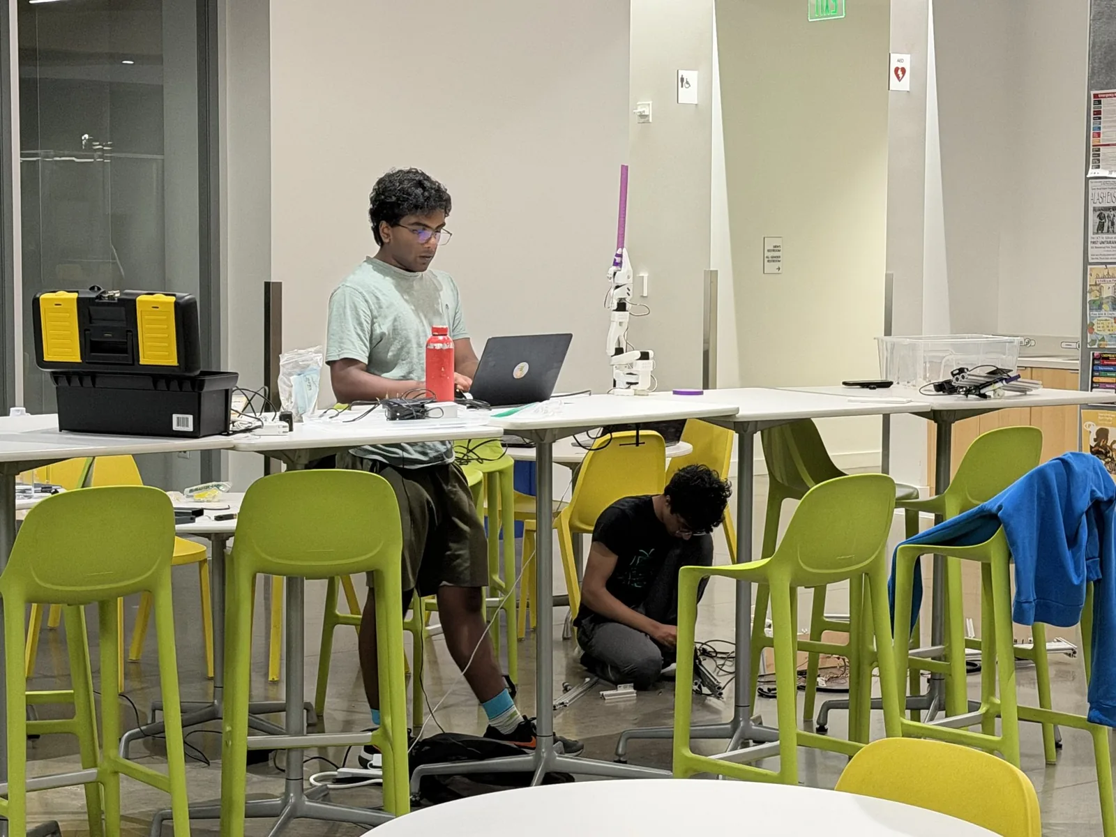 Two teammates working late in the lab, one at a laptop and one sitting on the floor