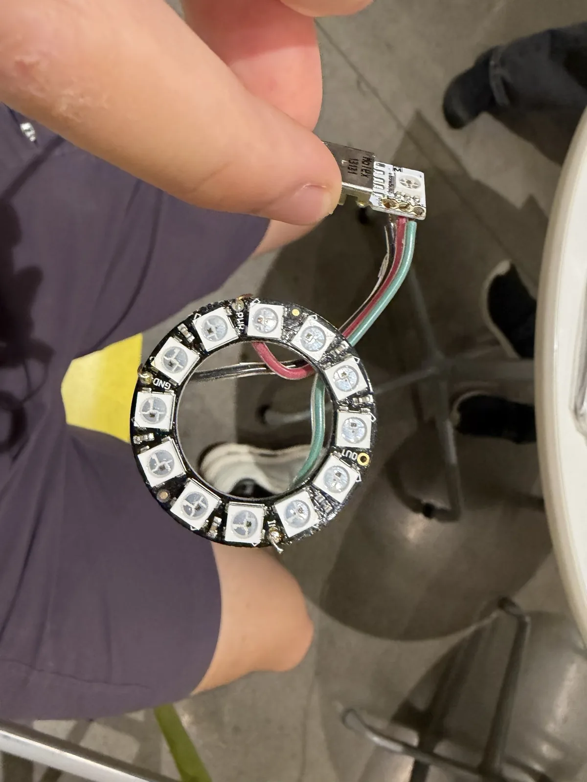 A hand holding a twelve-LED NeoPixel ring wired to a small board